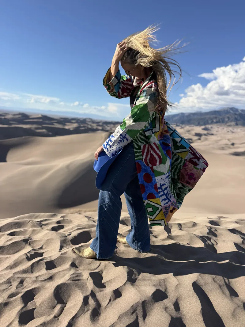 Wind lifts a woman's hair and a green, red and blue patchwork coat on a dune.