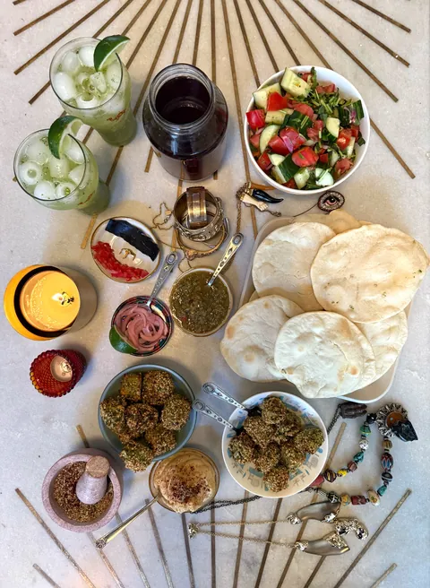 Overhead photograph of an Egyptian matchday spread of salads, flatbreads and falafel on a patterned cloth.
